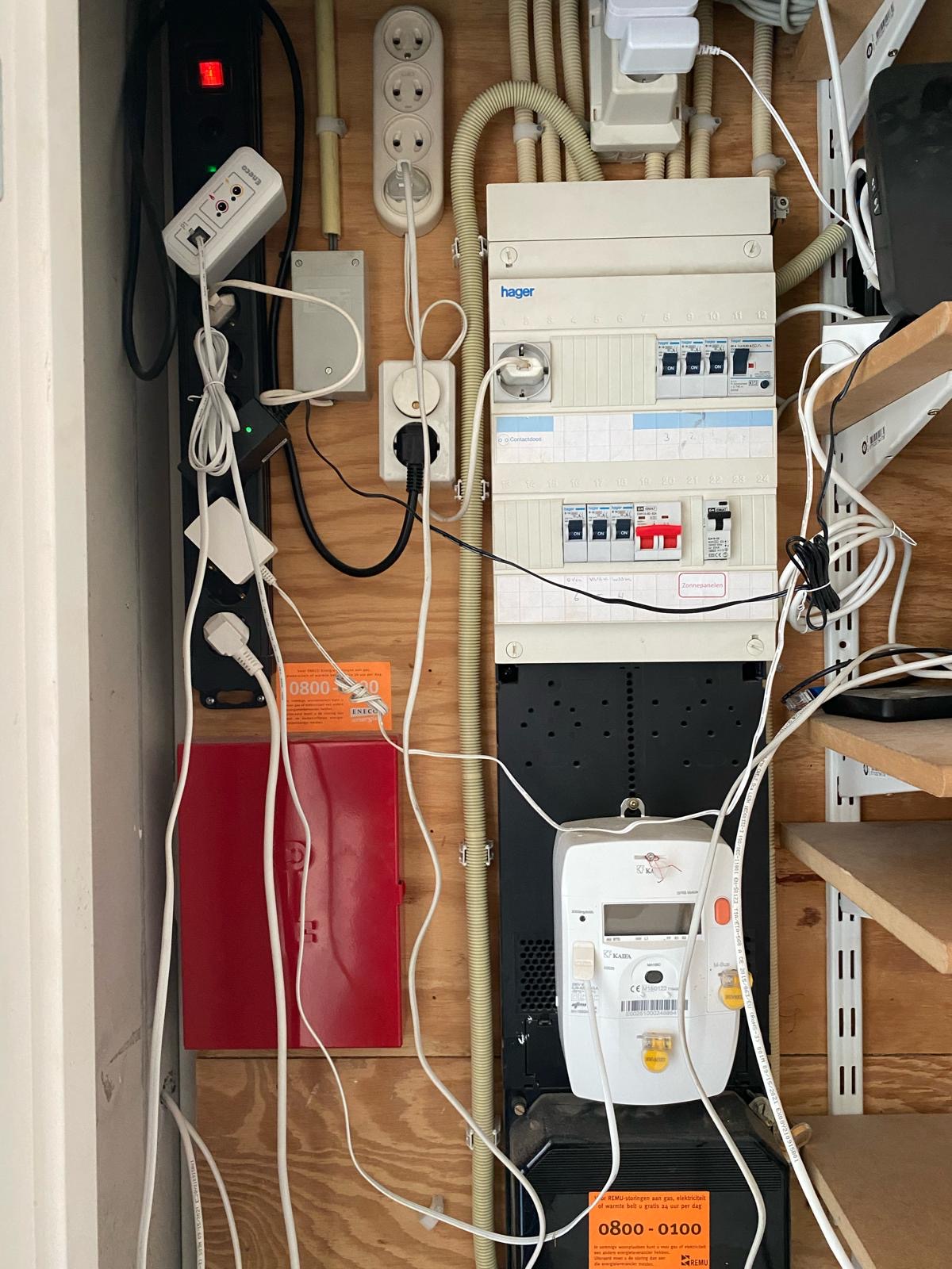 Oude, volle groepenkast met stekkerdozen en kabels ervoor